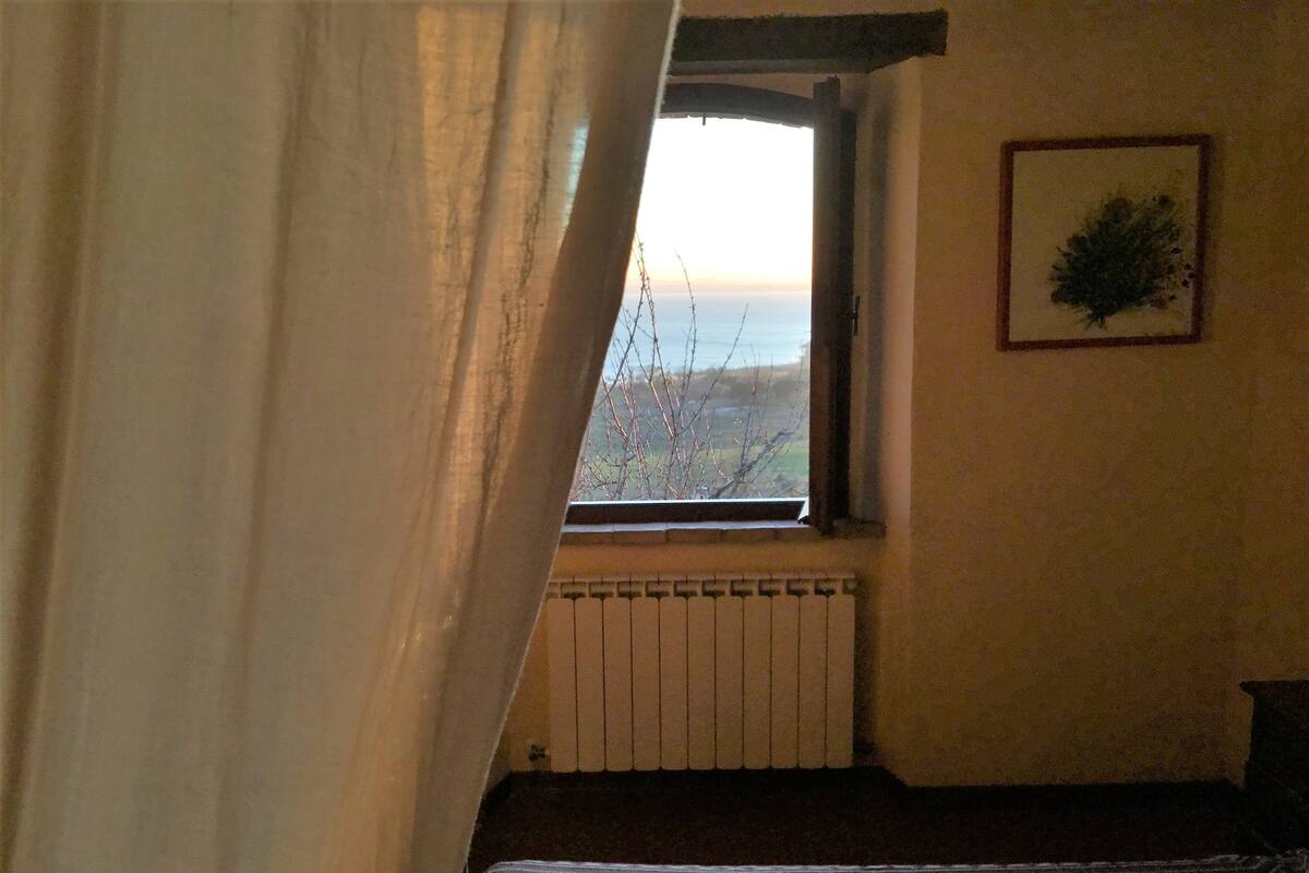 Ein Zimmer mit Fenster, Heizkörper, einem Bett mit Blumenmuster und einem gerahmten Bild an der Wand.