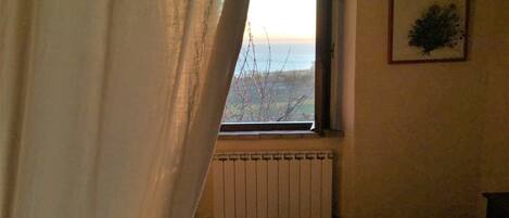 A room with a window, a radiator, a bed with a floral bedspread, and a framed picture on the wall.