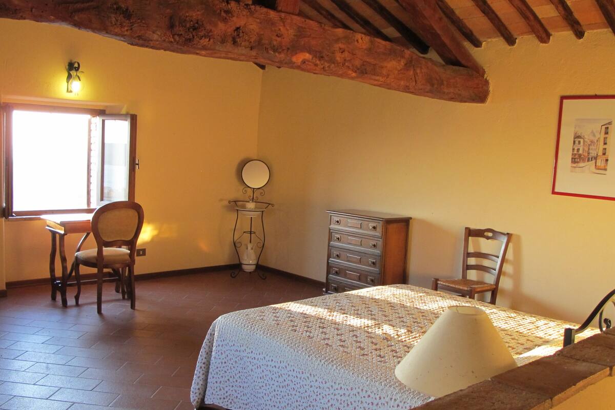 Ein Schlafzimmer mit Bett, Stuhl, Kommode, Spiegel und einem Fenster mit Sonneneinstrahlung.