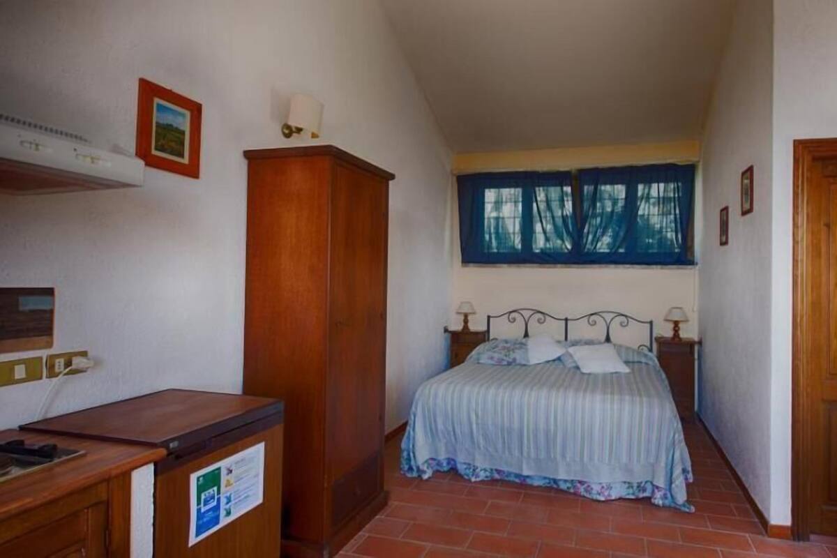 Ein Schlafzimmer mit Bett, Schreibtisch, Kleiderschrank und einem fenster mit Vorhängen.