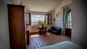 Ein Zimmer mit Bett, Tisch mit Stühlen, Meerblick und einem Vorhangfenster.
