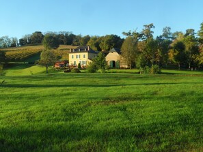 A large, open grassy field with a historic building featuring multiple windows and a stone structure.