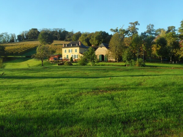 Un vaste champ herbeux, dégagé, avec un bâtiment historique doté de nombreuses fenêtres et d’une structure en pierre.