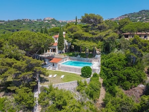 A villa with a swimming pool surrounded by lush greenery and a hilltop view.
