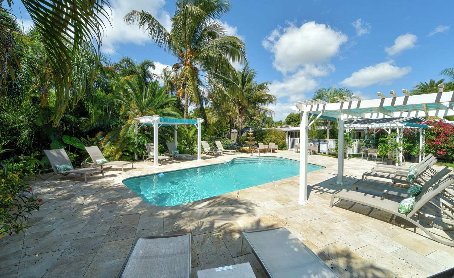 A rectangular swimming pool with lounge chairs and a gazebo, surrounded by palm trees and greenery.