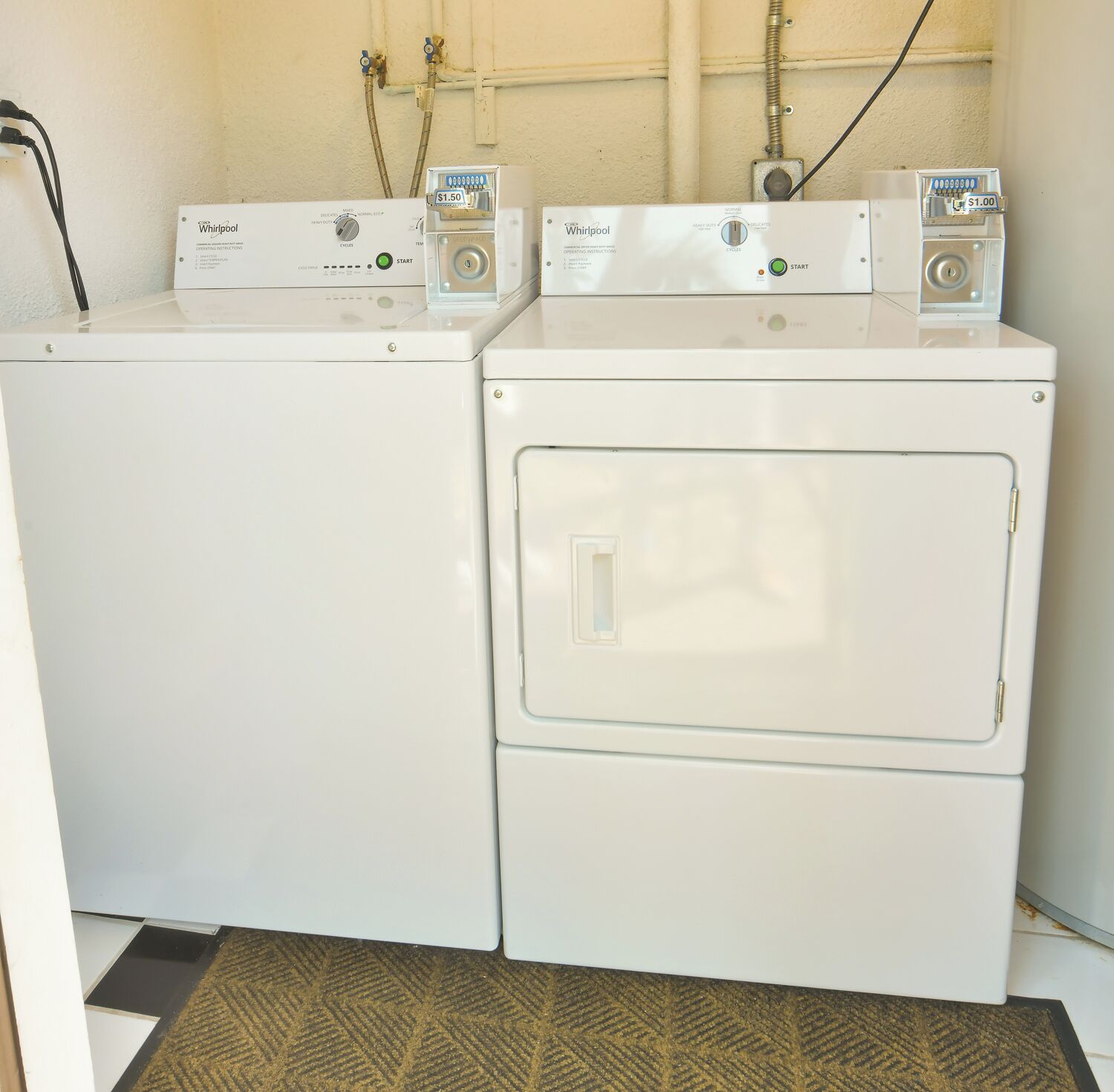 A laundry area with two stacked washers and dryers, a control panel, and visible plumbing.
