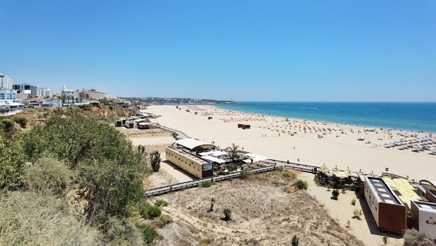 A beach with a row of beachside buildings, including a restaurant and a bus station. - Tropical Apartment with Terrace Praia da Rocha (Portimão)