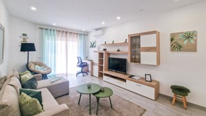 A modern living room with a sofa, coffee table, TV, and decorative items. - Tropical Apartment with Terrace Praia da Rocha (Portimão)