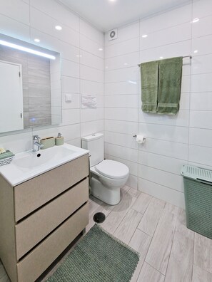 A modern bathroom with a white sink, mirror, and toilet. There is a green towel hanging on the wall and a green mat on the floor. - Tropical Apartment with Terrace Praia da Rocha (Portimão)