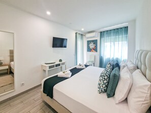 A modern hotel room with a large bed, a TV mounted on the wall, a small bedside table, and a window with curtains. - Tropical Apartment with Terrace Praia da Rocha (Portimão)
