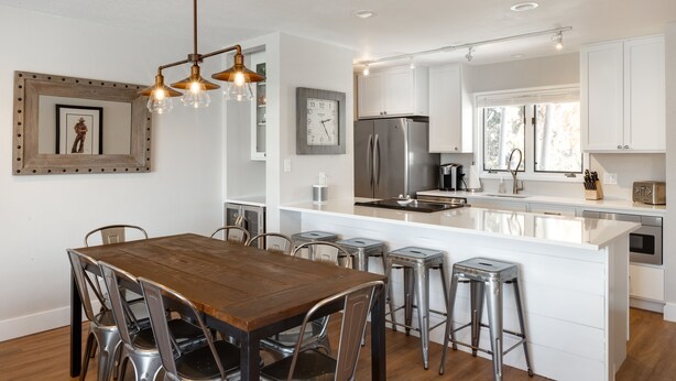 Una cocina moderna con armarios blancos, electrodomésticos de acero inoxidable y una mesa de comedor de madera con sillas metálicas.