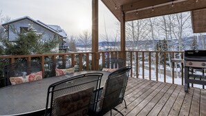 Un patio techado al aire libre con mesa y sillas, una parrilla y vistas a un paisaje nevado.