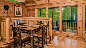 Ein Holzblockhaus-Interieur mit Esstisch, Stühlen und einem großen Fenster.