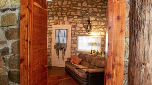 A cozy room with a stone wall, wooden door, and a leather sofa. - Victory Suite - Rustic Cabin (Hot Springs)