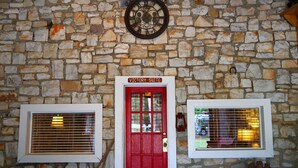 A stone wall with a red door labeled "Victory Suite," two windows with blinds, and a wall-mounted clock. - Victory Suite - Rustic Cabin (Hot Springs)