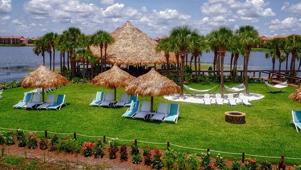 Zona junto a la piscina con sillones de descanso, sombrillas de paja y palmeras.