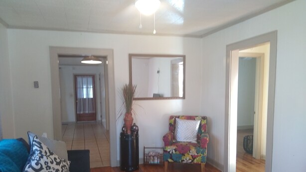 A living room with a wooden floor, a sofa, a colorful armchair, and a potted plant. There is a hallway leading to another room. - Charleston "Home-Away-from-Home" - Close to All Major Attractions! (North Charleston)