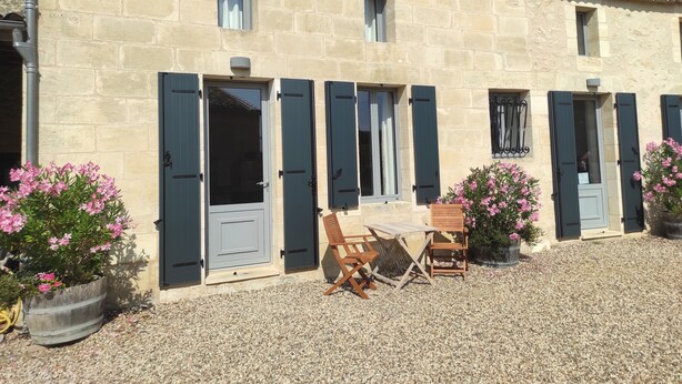 Un edificio de piedra con varias ventanas, una puerta y un patio de grava con mobiliario exterior.