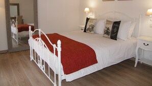 Una cama con dosel blanco con una manta roja, dos lámparas de noche y dos cuadros en la pared.