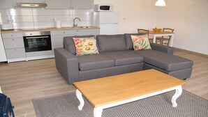 Una sala de estar moderna con un sofá gris, una mesa de centro de madera y una cocina al fondo.
