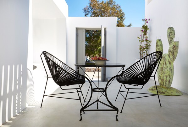 A modern outdoor seating area with two black wireframe chairs and a glass table, set against a white wall with a cactus sculpture and a potted plant. - Traditional Villa with Private Heated Pool (Santorini)