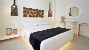 Un dormitori modern amb un llit gran, dues làmpades penjants fixades a la paret, una obra d'art de fusta, un mirall rodó i una petita taula de treball amb una cadira.
