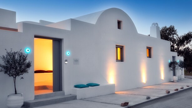 Un edifici modern blanc amb façana corbada, una porta que condueix a un interior càlid i petites finestres amb marcs il·luminats.