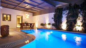 Una piscina amb un solàrium de fusta i zona de seients, envoltada de plantes i parets amb petites llums.