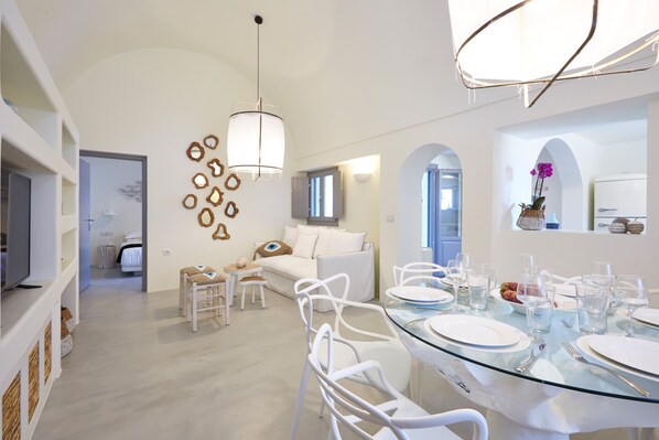 A modern dining area with a glass table set for six, white chairs, and a white sofa in the background. - Traditional Villa with Private Heated Pool (Santorini)