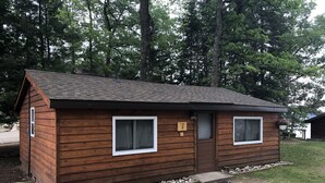 A small wooden cabin with two windows, a door, and a small porch area. - Cabin 6 Lake Cabins Resort on Fife Lake (Fife Lake)