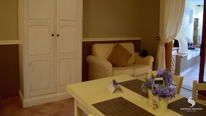 A room with a white wardrobe, a beige sofa, a table with a placemat and a vase of flowers, and an air conditioning unit on the wall.