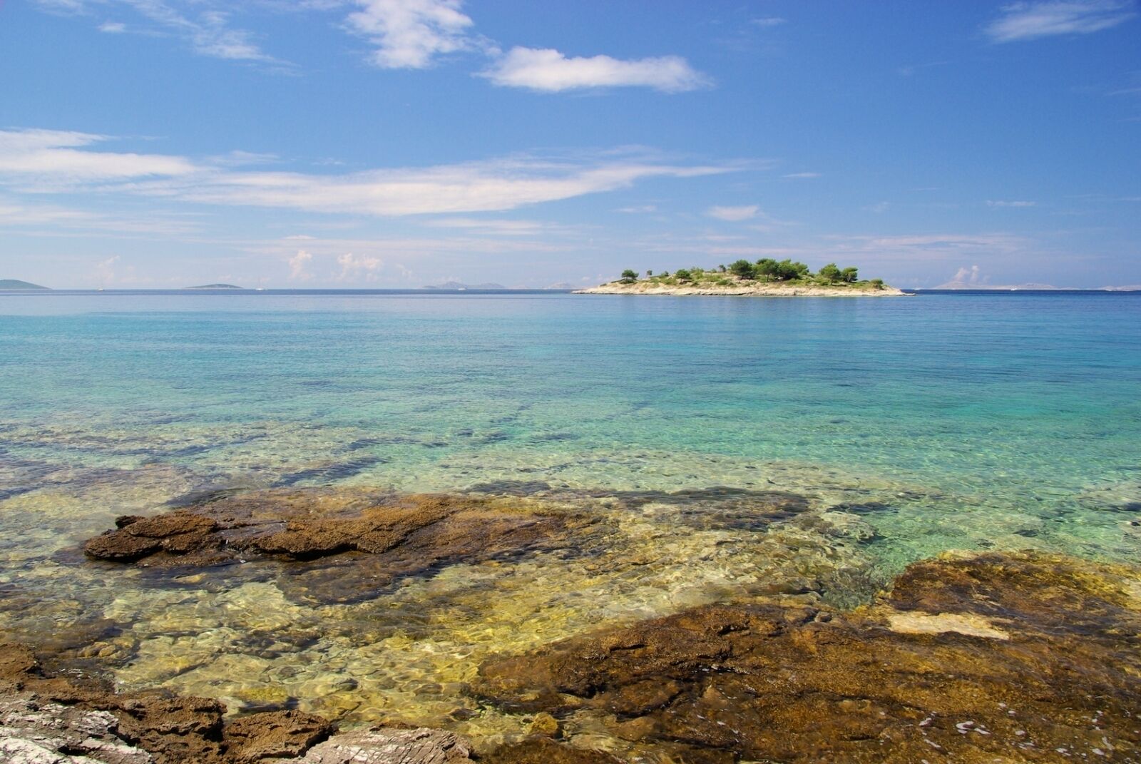 Una vista costera despejada, con rocas en primer plano y una isla distante.