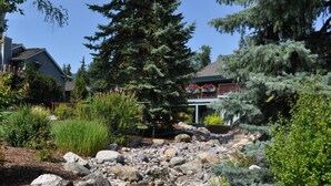 A residential area with a house, a small stream, and various trees. - Mountain Harbor #163 3 Bedroom Condo (Whitefish)