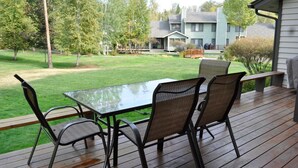 A wooden deck with a glass table and wicker chairs, overlooking a well-maintained lawn and neighboring houses. - Mountain Harbor #163 3 Bedroom Condo (Whitefish)