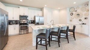 A modern kitchen with white cabinetry, stainless steel appliances, and a central island with bar stools. - Spacious Abode with Spillover Spa in Encore (Kissimmee)