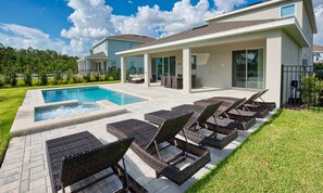Una casa moderna con piscina, mobiliario exterior y un césped bien cuidado.