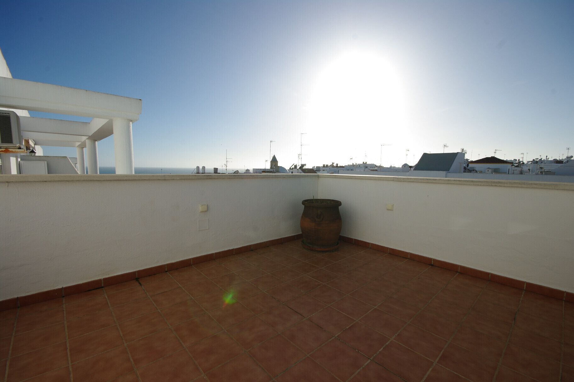 Een terras op het dak met uitzicht op zee, een grote terracotta pot en een witte constructie.