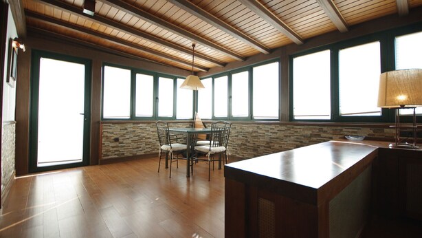 A spacious room with a high ceiling, large windows, a wooden floor, and a central table with chairs. - 192 - Ático El Cielo (Conil de la Frontera)