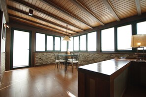 A spacious room with a high ceiling, large windows, a wooden floor, and a central table with chairs. - 192 - Ático El Cielo (Conil de la Frontera)