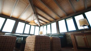 A room with a high ceiling, large windows, a green leather sofa, and a patterned armchair. - 192 - Ático El Cielo (Conil de la Frontera)