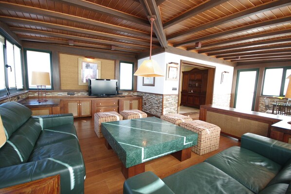 A spacious living area with a stone fireplace, leather sofas, a dining table, and a kitchen area with a TV. - 192 - Ático El Cielo (Conil de la Frontera)