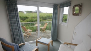 A room with a view of a grassy field, two wooden chairs, a small table, and a window with a mirror. - Roswidden on the cliff (Treyarnon Bay)