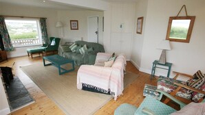 A cozy living room with a sofa, a small table, a bench, and a bed with a striped blanket. - Roswidden on the cliff (Treyarnon Bay)