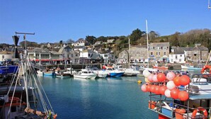 A harbor with boats docked, buildings in the background, and a clear sky. - Roswidden on the cliff (Treyarnon Bay)