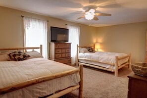 Een slaapkamer met twee houten bedden, een plafondventilator, een televisie en een dressoir.