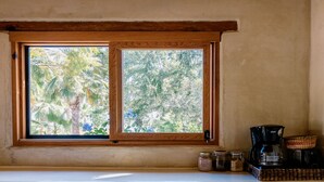 A window with a view of palm trees and a shelf with a coffee maker, jars, and a basket.