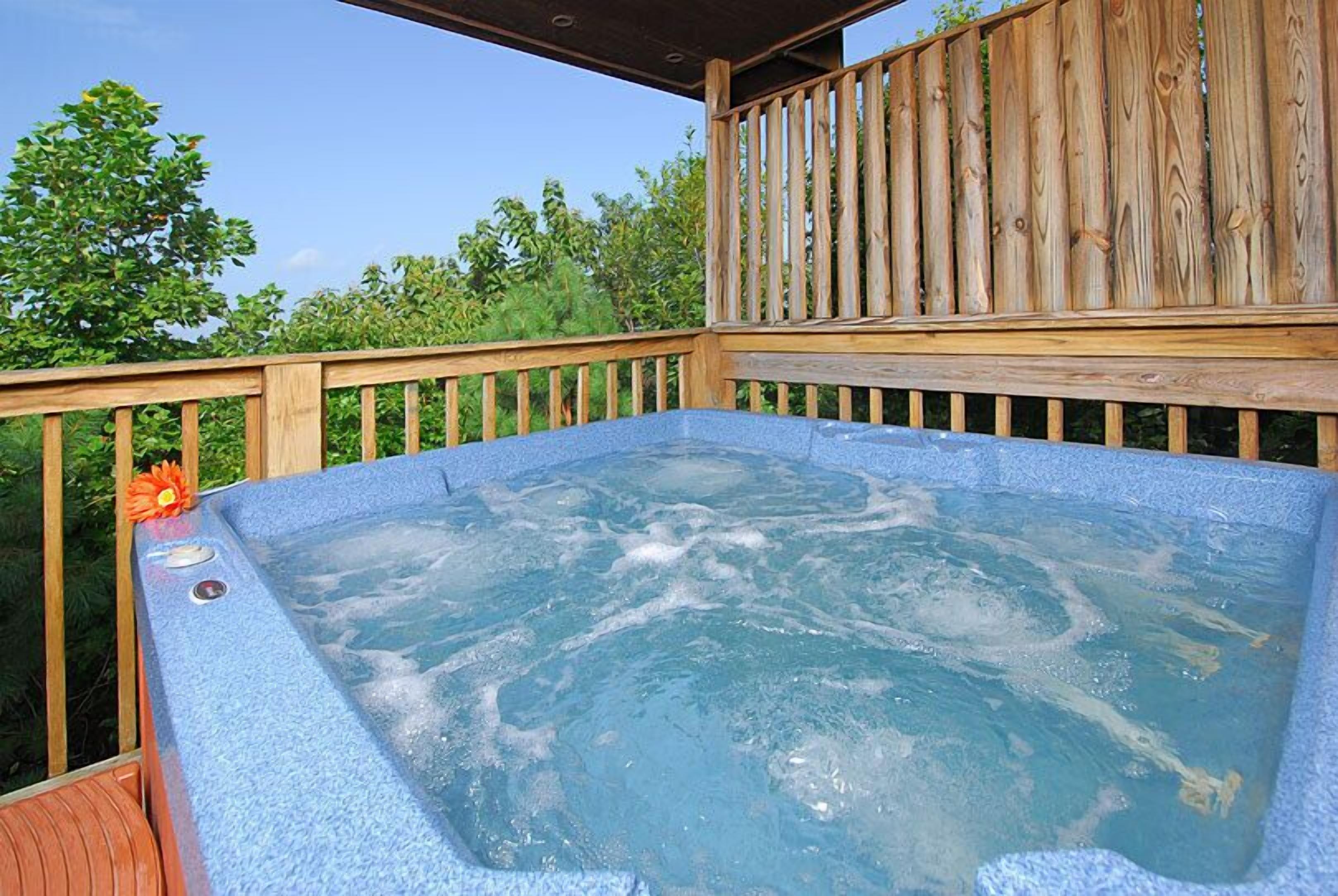 A hot tub on an outdoor deck with a wooden railing and greenery in the background.