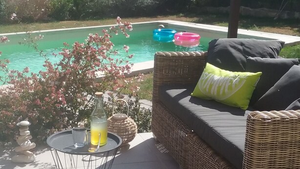 A wicker sofa with cushions and a glass table with a bottle and glasses.