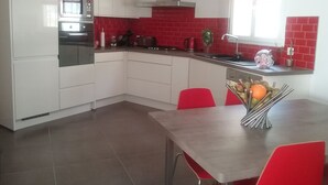 A modern kitchen with white cabinets, stainless steel appliances, and red accents.