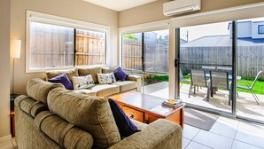 Un salon avec un canapé, une table basse et une vue sur le jardin à travers des portes vitrées.